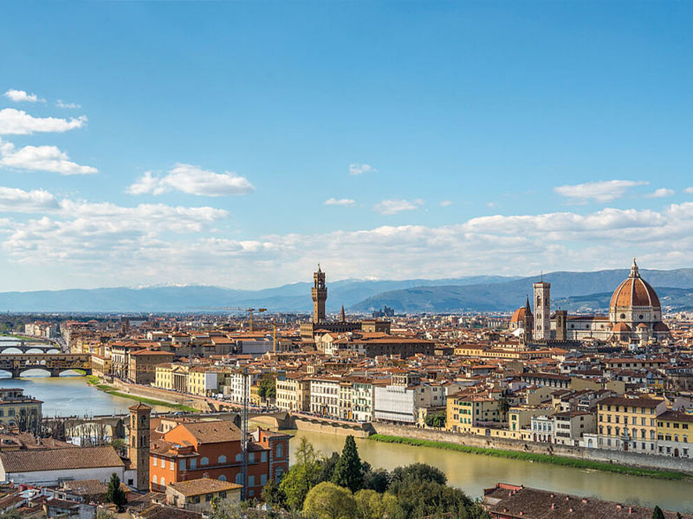 Weitwinkel-Panorama von Florenz mit Blick auf den Dom (Santa Maria del Fiore), den Fluss Arno und die historische Stadtmitte unter blauem Himmel.