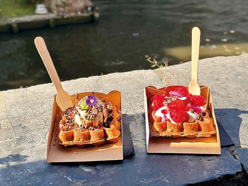 Zwei belgische Waffeln mit Erdbeeren und Eis auf einer Steinmauer am Kanal in Brügge, Belgien.