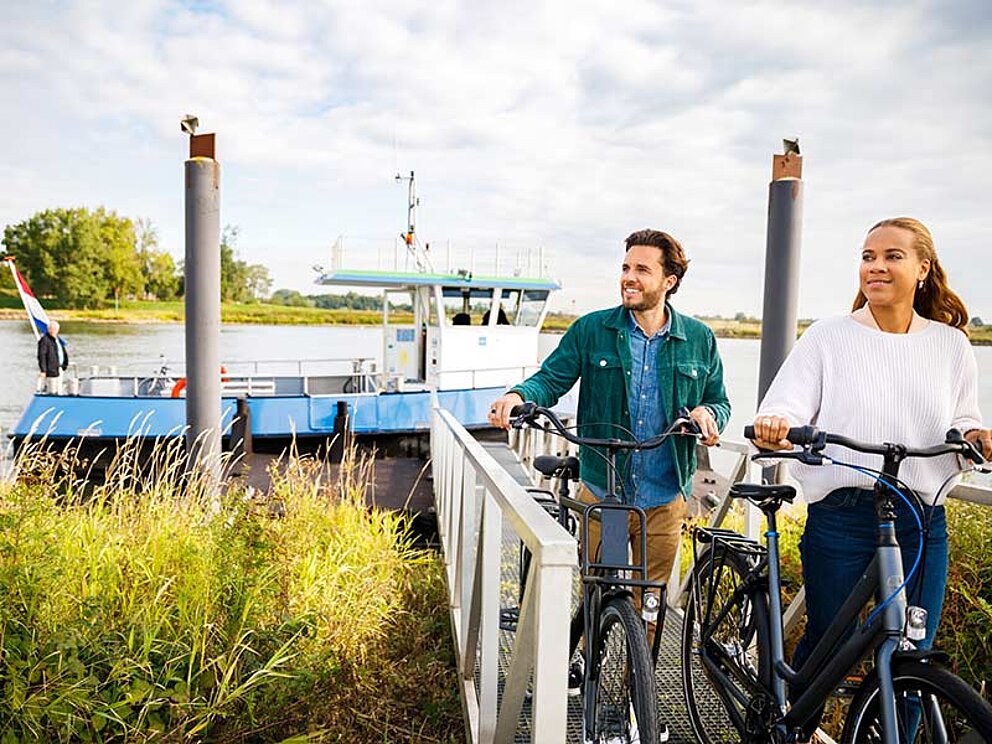 2 Radfahrer schieben ihre Räder vom Schiff über einen Steg richtung Land