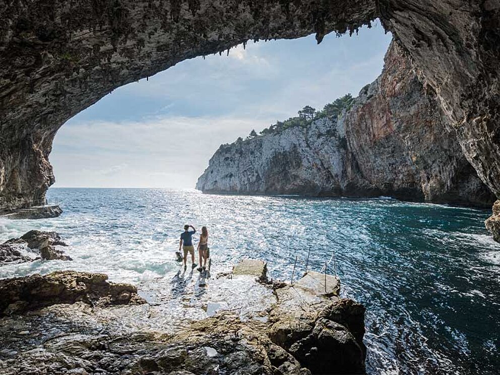 Blick aus einer beeindruckenden Meereshöhle auf das türkisfarbene Wasser und die schroffen Felsklippen der Küste Apuliens, Italien.