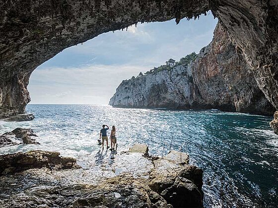 Blick aus einer beeindruckenden Meereshöhle auf das türkisfarbene Wasser und die schroffen Felsklippen der Küste Apuliens, Italien.