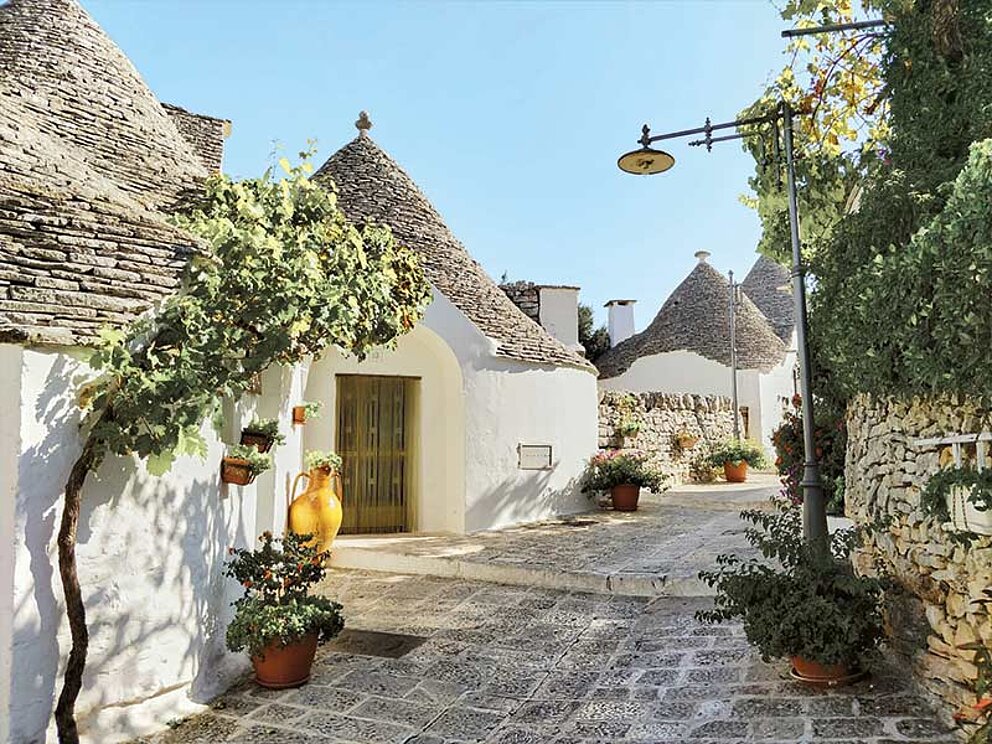 Traditionelle weiße Trulli-Häuser mit kegelförmigen Steindächern in einem malerischen Dorf in Apulien, Italien.