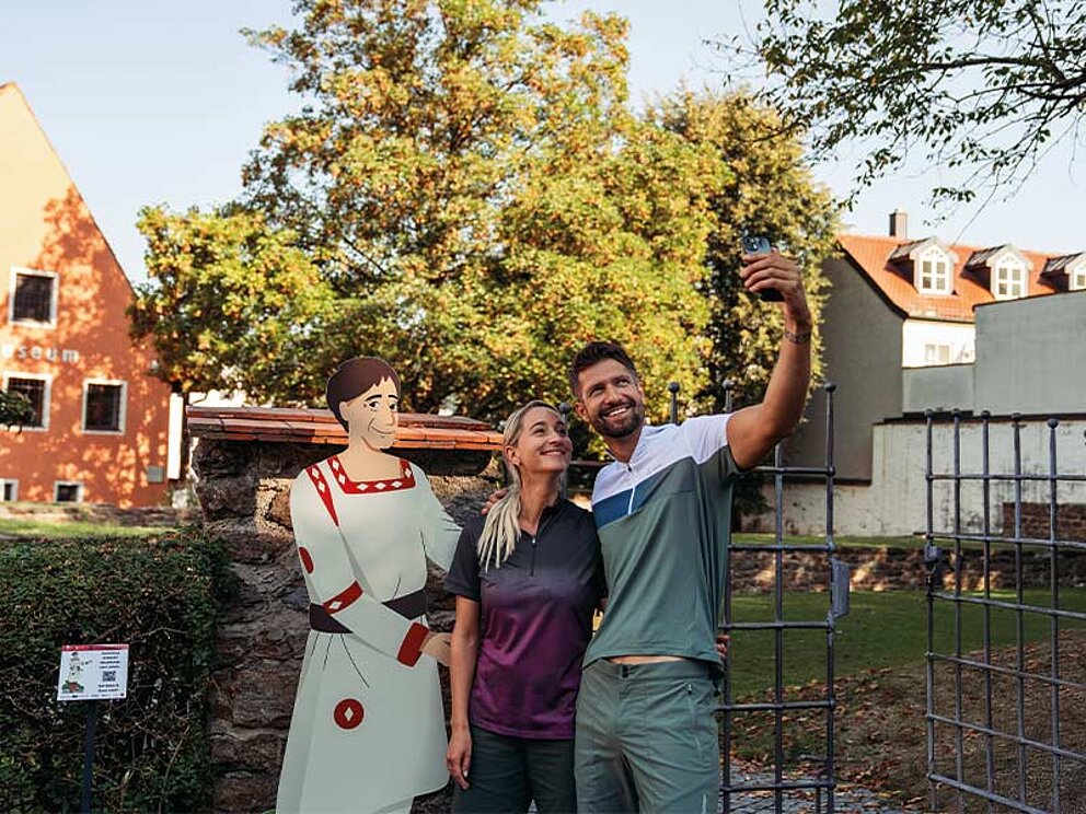 Ein Paar macht ein Selfie mit einer lebensgroßen Figurendarstellung einer Römerin im Kastell Biotro in Passau, Deutschland.