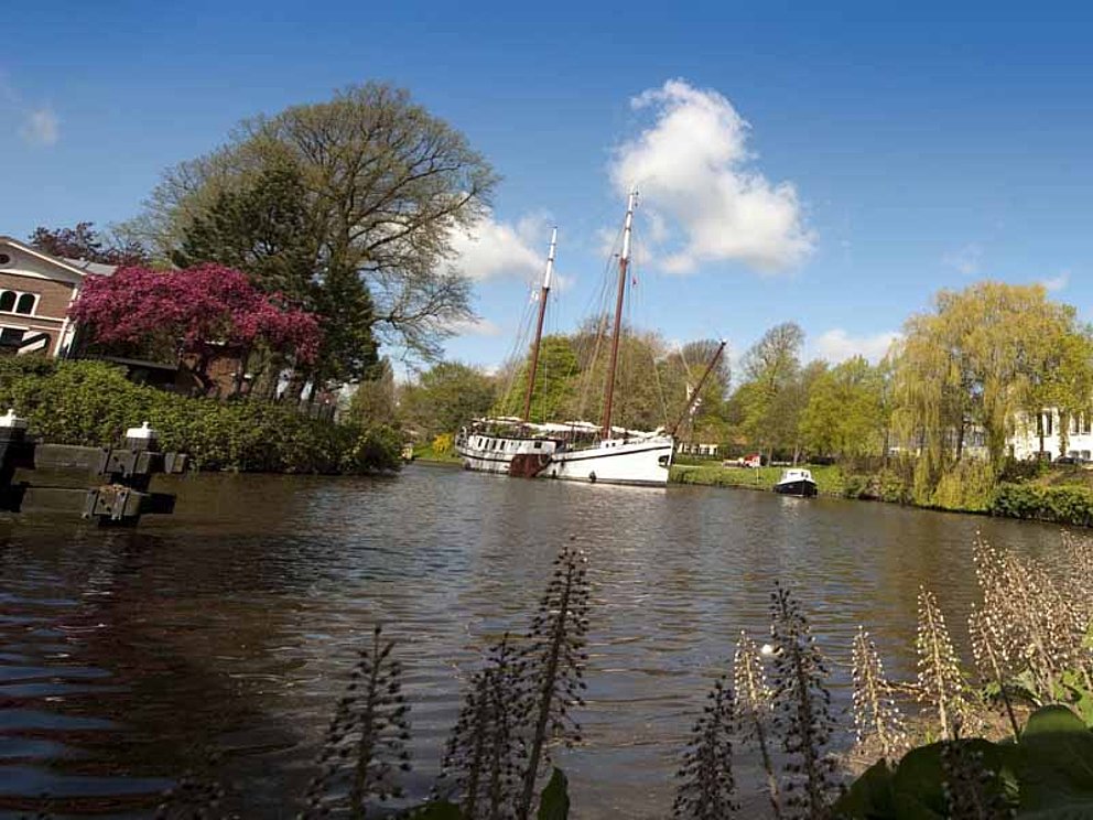 Blick auf den Fluss von Leeuwarden in Holland. Ein Schiff fährt langsam vorbei. An den Ufern stehen viele Bäume.