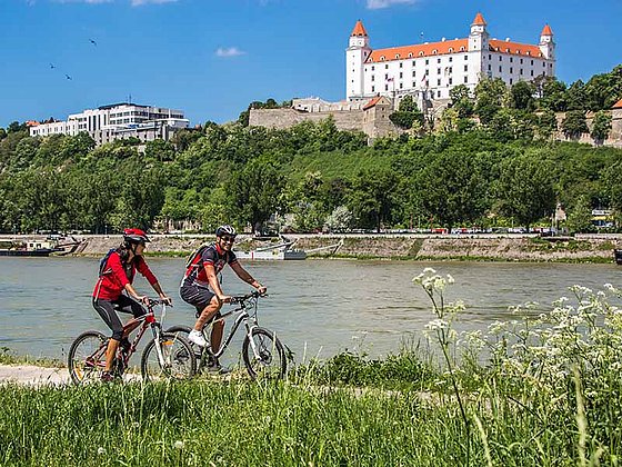 zwei Radfahrer unterwegs am Radweg in Bratislava mit Burg im Hintergrund