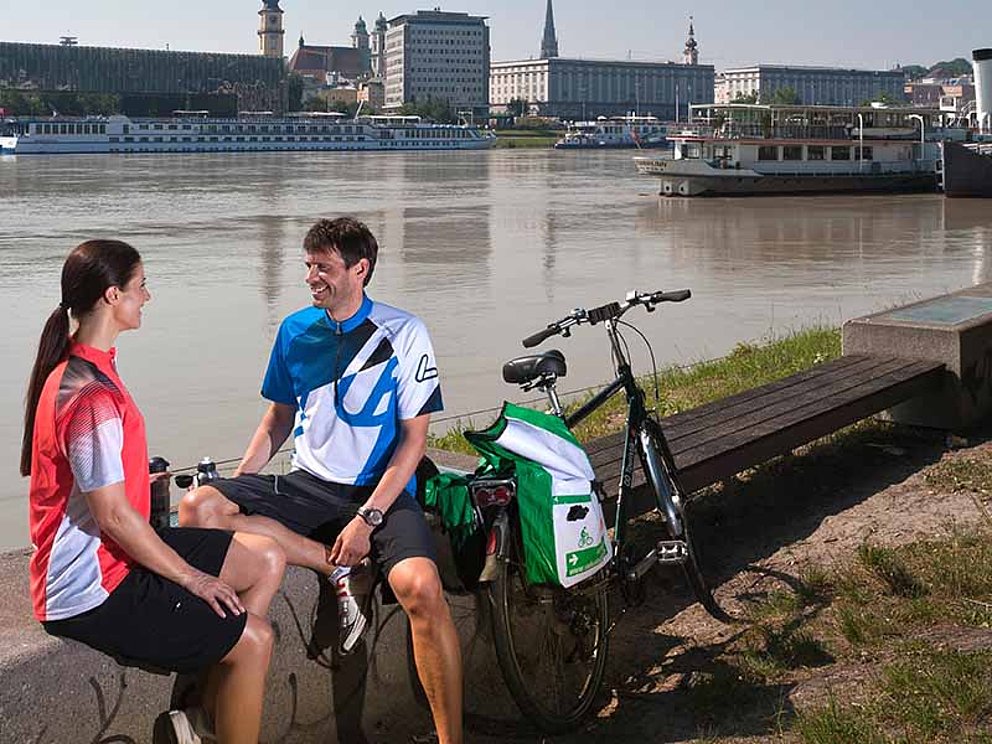 Zwei Radfahrer machen Pause entlang des Donauradweges in Linz