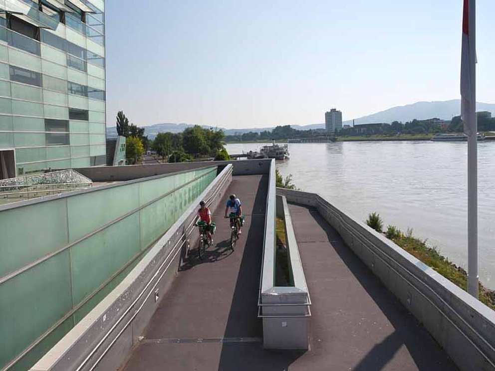 2 Radfahrer fahren vorsichtig die Rampe vom Ars Electronica Center zur Donau hinunter.