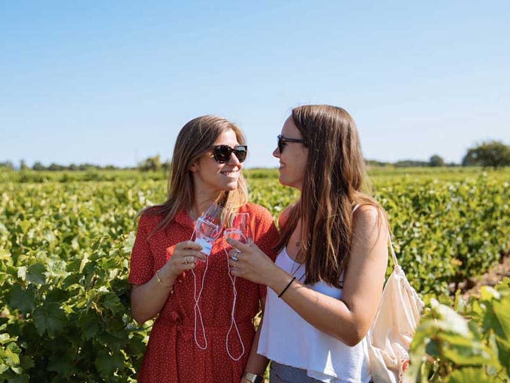 2 junge Frauen trinken ein Glas Wein inmitten eines Weingartens