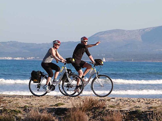 Radfahrer fahren auf einem Sandstrand in Mallorca entlang.