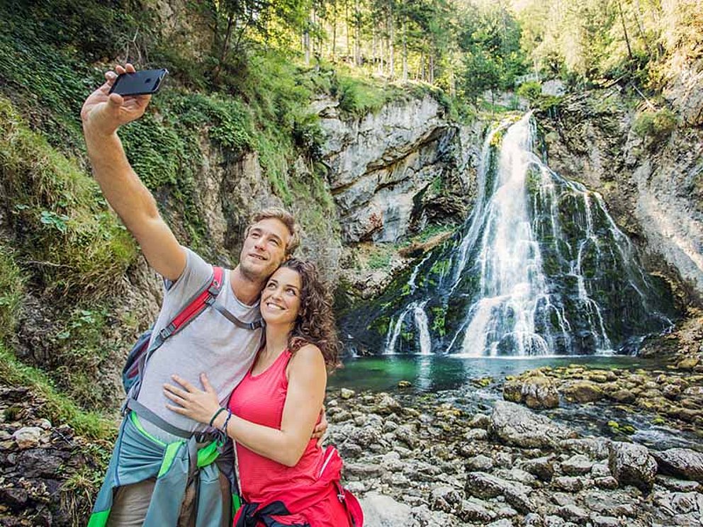 a couple takes a selfie in front of a waterfall