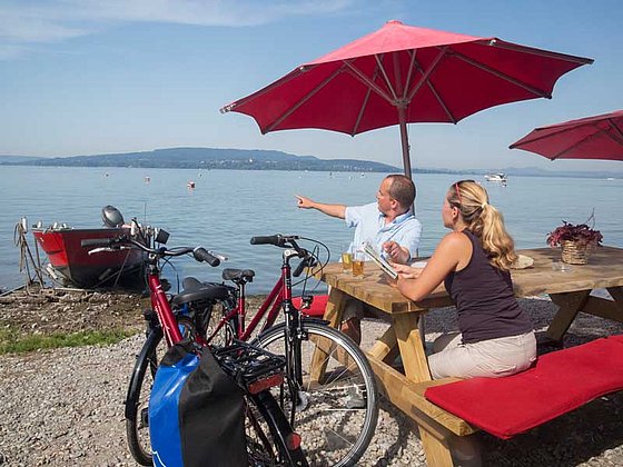 Ein Ehepaar entspannt am Bodenseeufer unter einem Sonnenschirm