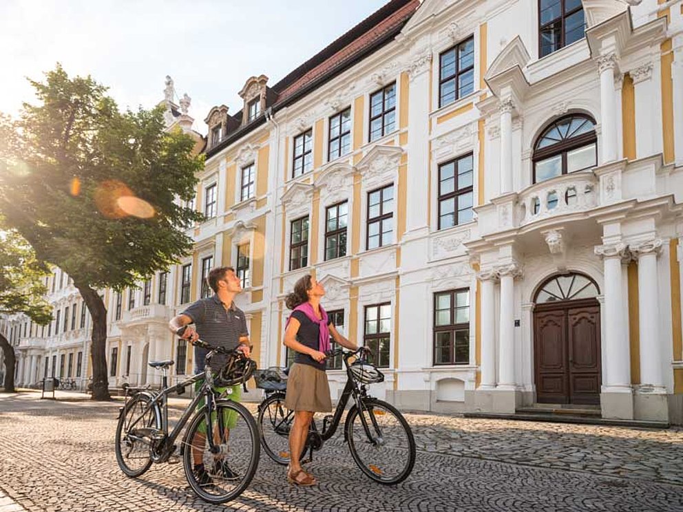 Mann und Frau schieben ihre Fahrräder durch die Altstadt von Magdeburg