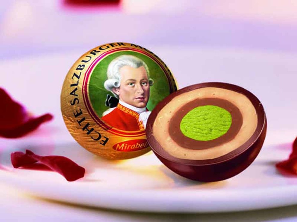 eine aufgeschnittene Mozartkugel mit Pistazienmasse im Kern, Nougatring, Marzipanring und Kuvertüre aus dunkler Schokolade.