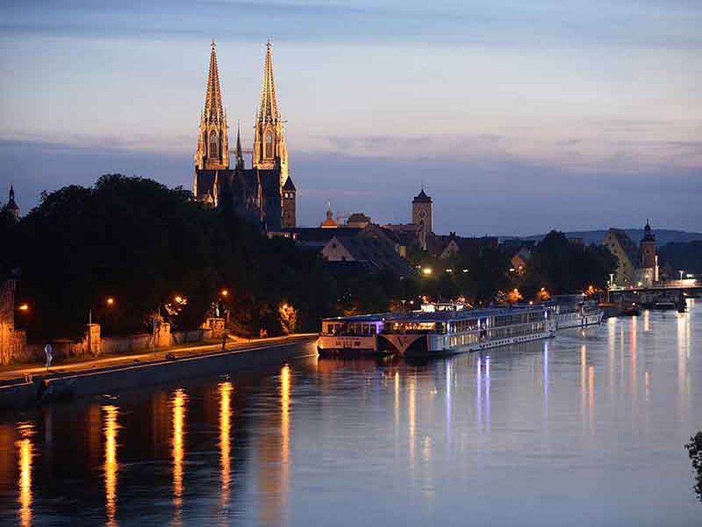 Blick auf beleuchtetes Regensburg mit Dom an der Donau bei Nacht