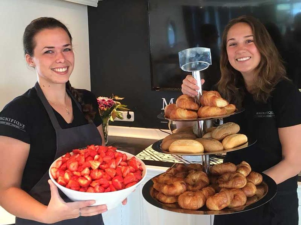 2 junge Frauen präsentieren Erdbeeren und Gebäck für das Frühstücksbuffet