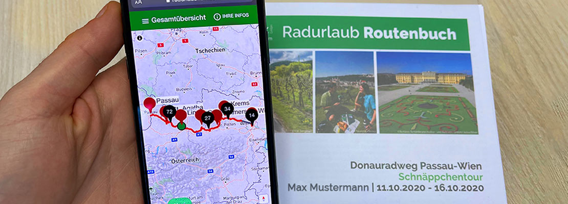 Smartphone mit geöffnetem Radurlaub-Navi. Routenbuch im Hintergrund