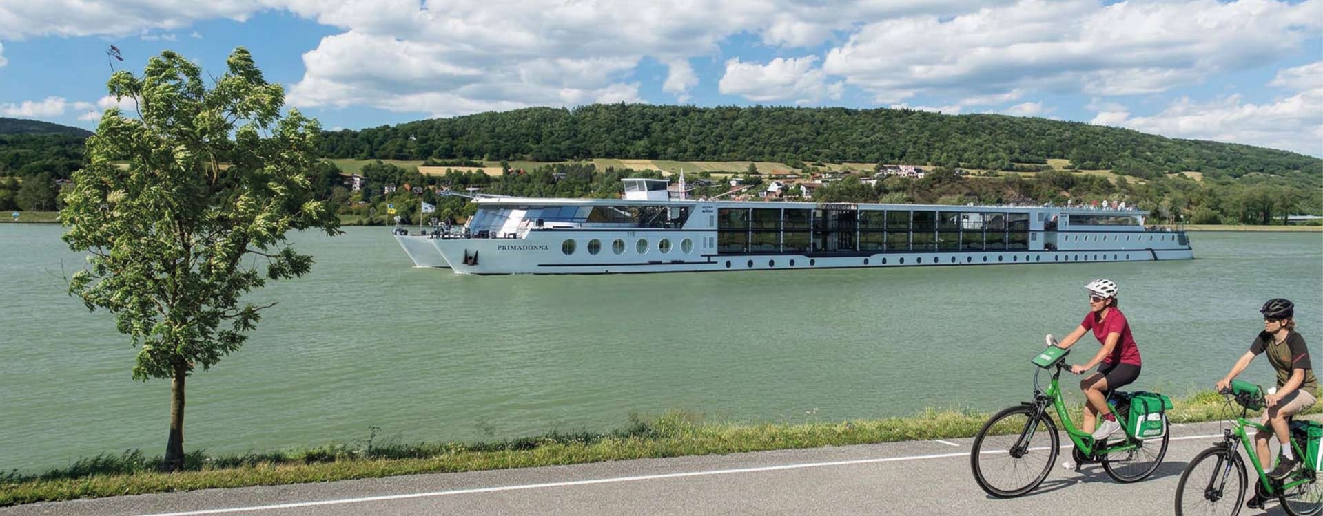 2 Radfahrer am Ufer, im Hintergrund die MS Primadonna auf der Donau