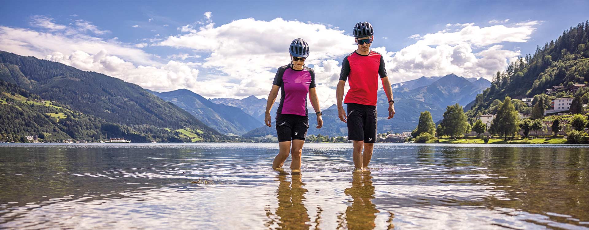 ein Paar mit Radkleidung kühlt sich die Beine im Zeller See ab.